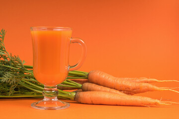 Fresh carrots with herbs and a glass of smoothies on an orange background.