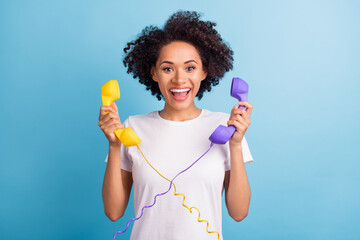 Portrait of young cheerful excited amazed african woman hold two cord telephones isolated on blue color background