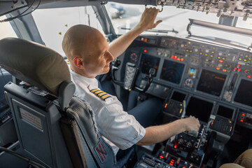 High angle view of professional pilot sitting in an airplane cabin, ready for takeoff. Aircraft, aircrew, occupation concept - obrazy, fototapety, plakaty