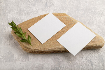 White paper business card, mockup with stone and boxwood branch on gray concrete background. side view, copy space.