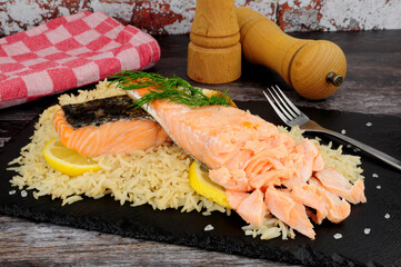 Two cooked salmon fillets with rice and dill herb garnish on a slate serving board