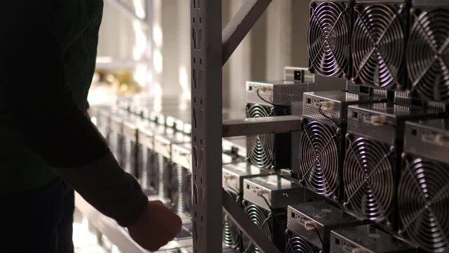 Loader brings in bitcoin miners to steel shipping container warehouse. Mover puts down mining equipment to stand racks for cryptocurrency mining farm. Workers carry loads to storage.