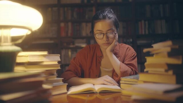 Young asian student reading interesting book, staying at library late at night