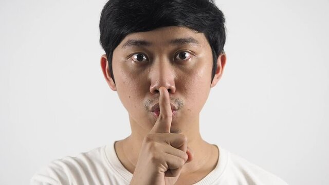 Close up asian man gesture shush show finger at his mouth slience sign looking at camera portrait white isolated