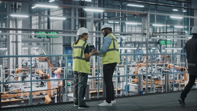 Male Specialist and Female Car Factory Engineer in High Visibility Vests Using Laptop Computer. Automotive Industrial Manufacturing Facility Working on Vehicle Production. Diversity on Assembly Plant.