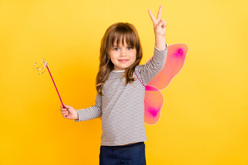 Photo of funky small blond hair girl hold stick show v-sign wear wings wand striped shirt isolated...