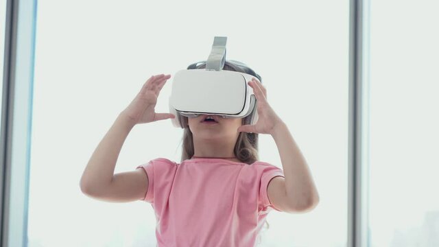 The girl touches and takes off her virtual reality glasses, stands against the background of the window. High quality 4k footage