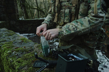 Portrait of airsoft player in professional equipment loads a gun with bullets in the forest. Soldier with weapons at war