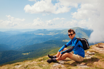 Trip to Carpathian mountains. Happy man hiker with backpack resting on top of Hoverla. Traveling in summer Ukraine