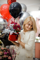 Happy woman with round box of flower arrangement in her hands. Red and silver colors.