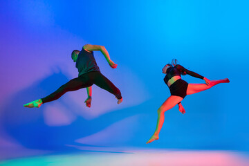 Fototapeta na wymiar Stylish sportive caucasian couple, male and female dancer dancing contemporary dance on colorful gradient blue pink background in neon light.