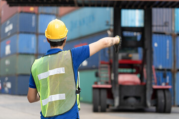 Foreman uses hand signal to forklift driver loading containers box from Cargo freight ship at Cargo...