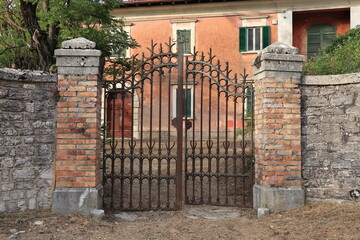 Red House with Green Shutters and Iron Gate Entrance with Stone Pillars in Rural Village, Italy