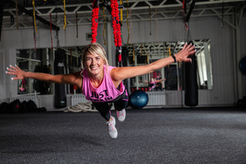 Bungee fitness. Training on loops. A beautiful sports woman in a pink tracksuit trains in the gym with the help of special loops. Poses in limbo - obrazy, fototapety, plakaty