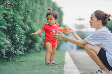 baby standing in outdoor to practice balance in development according to the age of the child with mother helping daughter support