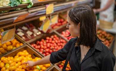 Woman chooses and purchases fresh ripe organic tomatoes in vegetable department of supermarket