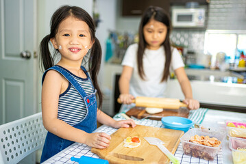 Asian girl in casual dress having fun while make pizza with prosciutto, tomato, cheese, vegetables in home kitchen. family and relationship concept