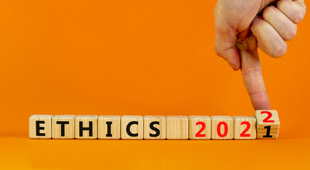 2022 ethics and new year symbol. Businessman turns wooden cubes and changes words 'ethics 2021' to 'ethics 2022'. Beautiful orange background, copy space. Business, 2022 ethics and new year concept.