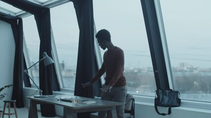 Young Afro-American businessman closing laptop, turning off desk lamp, taking jacket and bag and then leaving office after workday