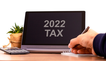 2022 tax new year symbol. Tablet with words '2022 tax'. Businessman hand with pen, house plant. Copy space. Beautiful white background. Business, 2022 tax new year concept, copy space.