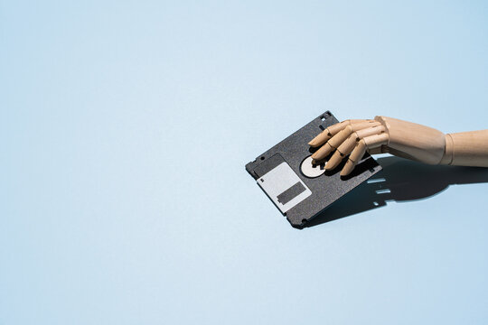 Wooden hand with floppy disk on blue table