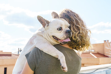 Unrecognizable woman dog lover hugging baby bulldog. Horizontal view of woman with pet. Lifestyle with animals outdoors.