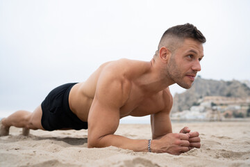 Strong sportsman doing plank exercise during workout on beach