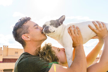 Intimate moment of couple kissing dog outdoors at sunset. Horizontal view of couple playing with pet.