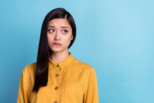 Photo of young attractive asian girl unhappy upset worried nervous bite lips fail look empty space isolated over blue color background