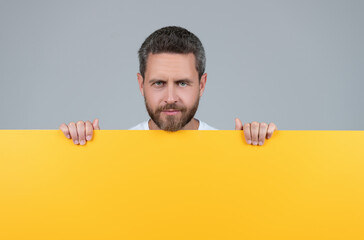 mature bearded man behind yellow paper with copy scape, advertising