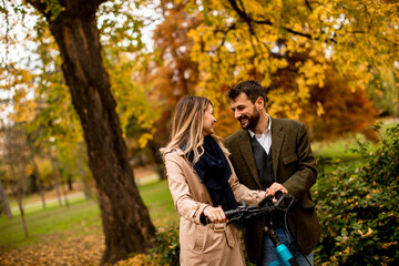 Fototapeta premium Young couple in the autumn park with electrical bicycle
