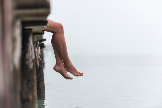 Crop woman sitting on pier in foggy morning