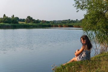 Adult Caucasian woman on lakeshore looking into distance. Portrait of lonely and pensive woman. Concept of reflection, use of the day and the moment. Beatiful landscape.