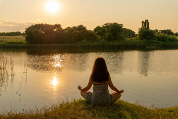 Woman sitting in lotus position in meditation on a hill overlooking rural landscape, at sunset....