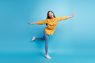 Full length photo of cool young brunette lady play wear yellow shirt jeans sneakers isolated on blue color background