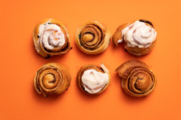 Obraz premium Freshly baked cinnamon buns on an orange background top view. patern. copy space