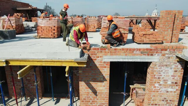 Workers on the construction of a house laying red bricks. Builders are building a brick wall of a high-rise building.