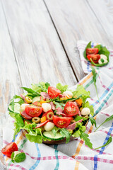 Fresh juicy salad with ham, tomatoes, lettuce, outlets in a wooden plate on a white wooden background. Space for text. High quality photo