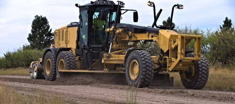 Road grader smoothing a dirt road in a rural area.