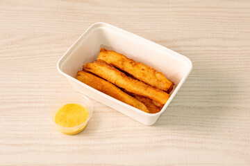 Fried cassava strips in a home delivery container with sweet curry sauce