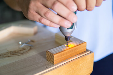 Close up view of a man's hands using an electric screwdriver to anchor a wooden leg