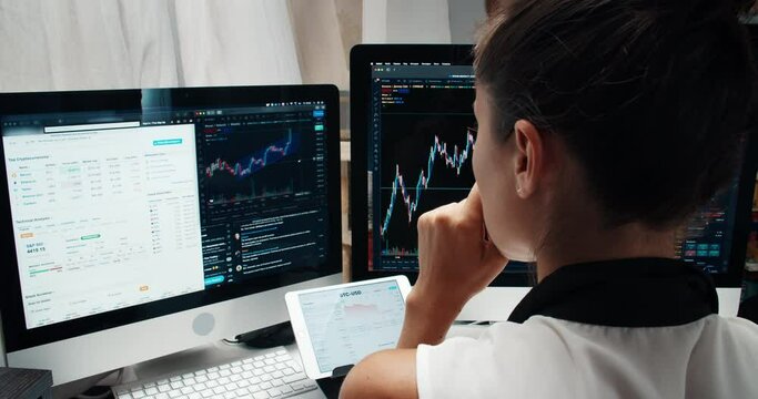 Young frelancer woman from back analyzing financial graphs working at home during the pandemic wide open footage. Caucasian using two screens and one tablet