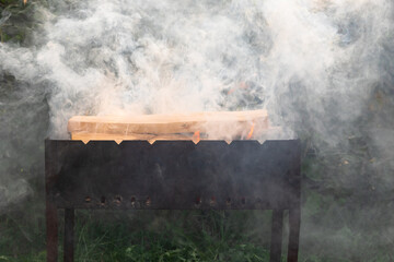 Metal brazier with burning wood in nature. A lot of swirling smoke. Bonfire with red flames. Selective focus. Close-up
