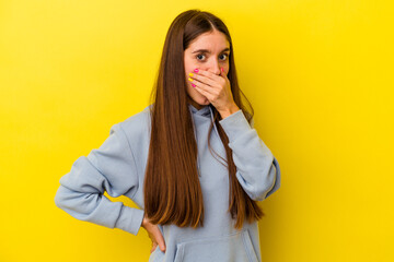 Young caucasian woman isolated on yellow background covering mouth with hands looking worried.