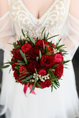 The bride holds a beautiful bouquet of red roses and peonies in her hand.