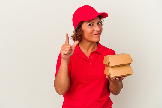 Middle age delivery woman taking burguers isolated on white background showing number one with finger.