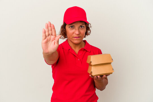 Middle age delivery woman taking burguers isolated on white background standing with outstretched hand showing stop sign, preventing you.