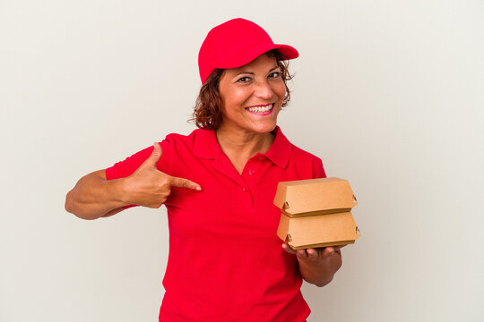 Middle age delivery woman taking burguers isolated on white background person pointing by hand to a shirt copy space, proud and confident