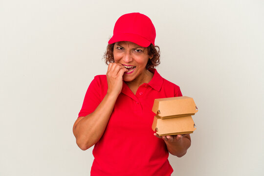 Middle age delivery woman taking burguers isolated on white background biting fingernails, nervous and very anxious.