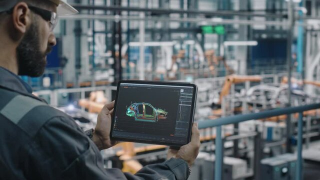 Car Factory Engineer in Work Uniform Using Tablet Computer with Digital 3D CAD Vehicle Blueprint. Male Specialist in Automotive Industrial Manufacturing Facility Working on Automobile Production.
